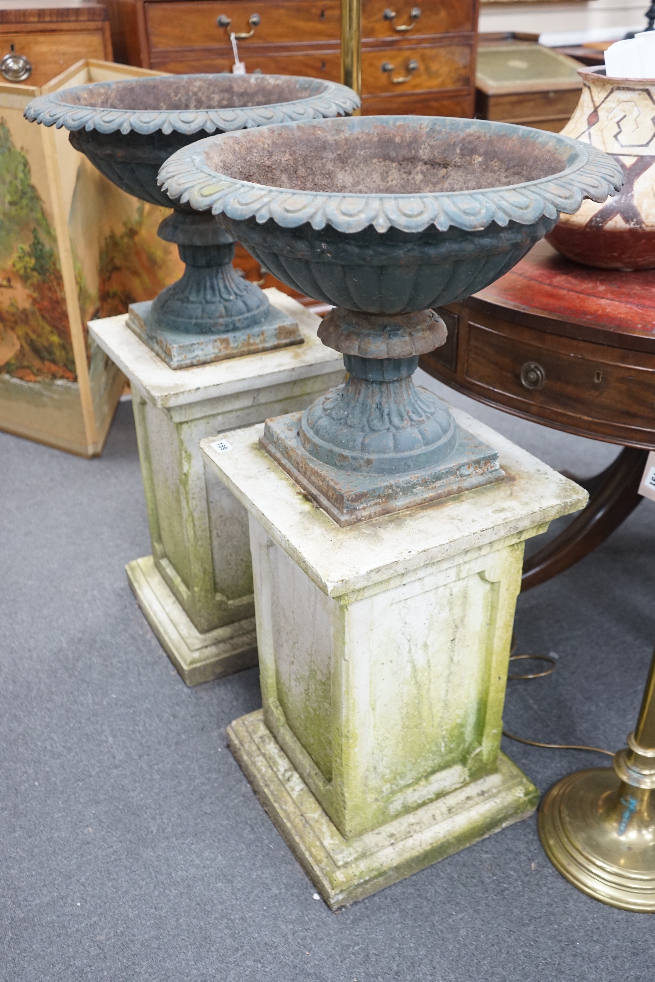 A pair of Victorian painted cast iron campana garden urns on square stone plinths, diameter 51cm, height including plinths 99cm